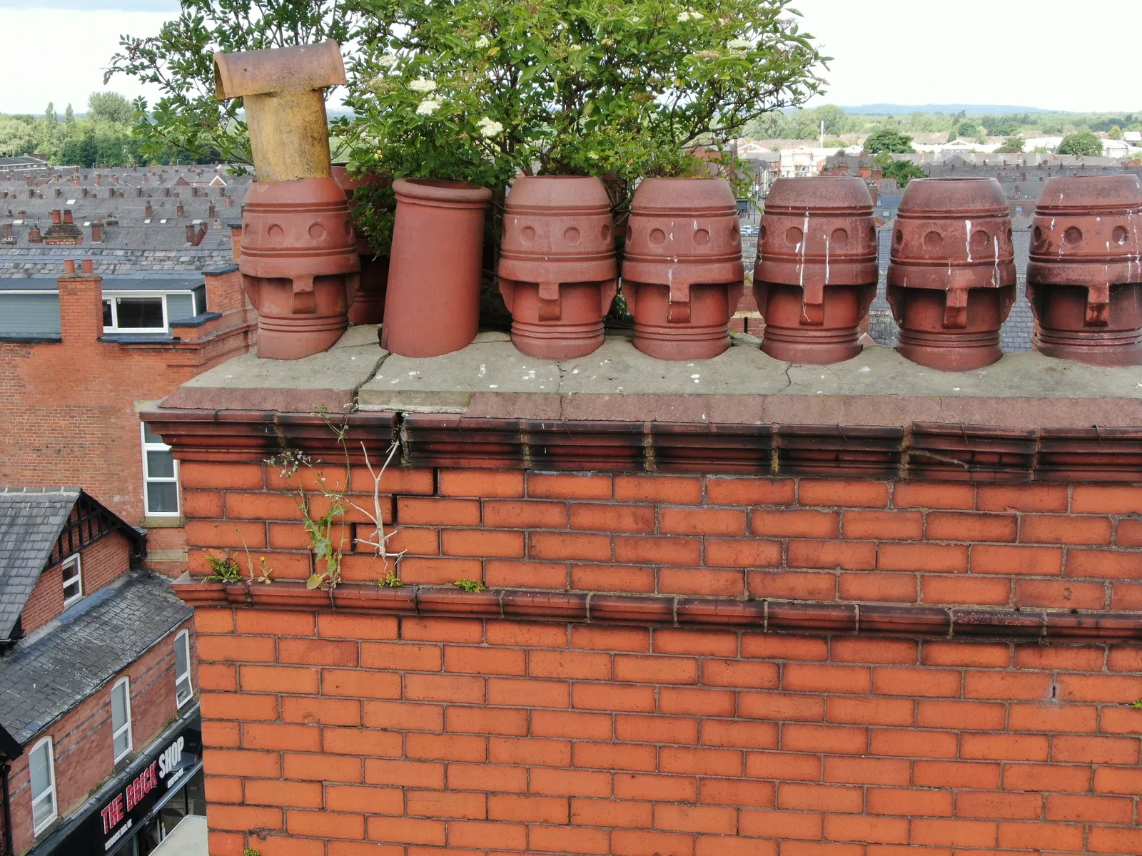 Brick chimney stack with clay pots and plant growth in the mortar